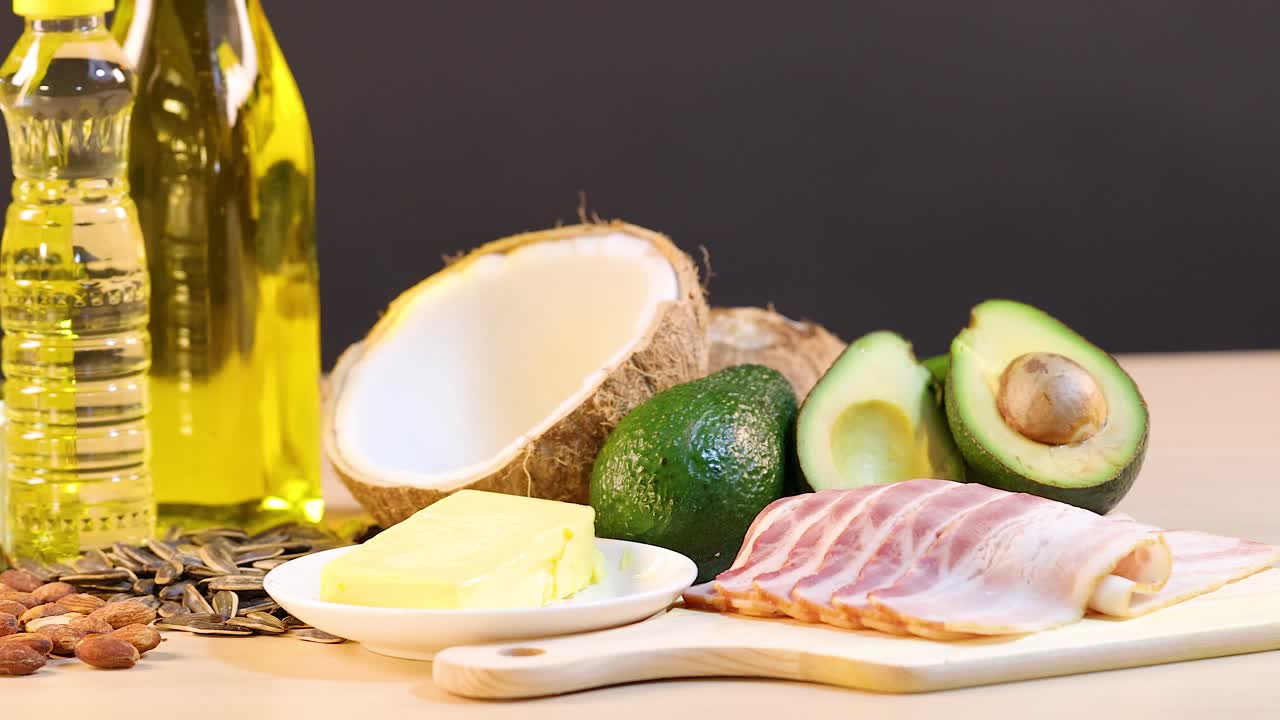 A variety of healthy fats including oils, nuts, and avocados arranged on a wooden table with bright lighting