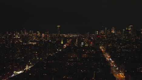 Forwards-fly-above-metropolis-at-night.-Multistorey-apartment-houses-in-urban-borough-ad-high-rise-buildings-in-background.-Manhattan,-New-York-City,-USA