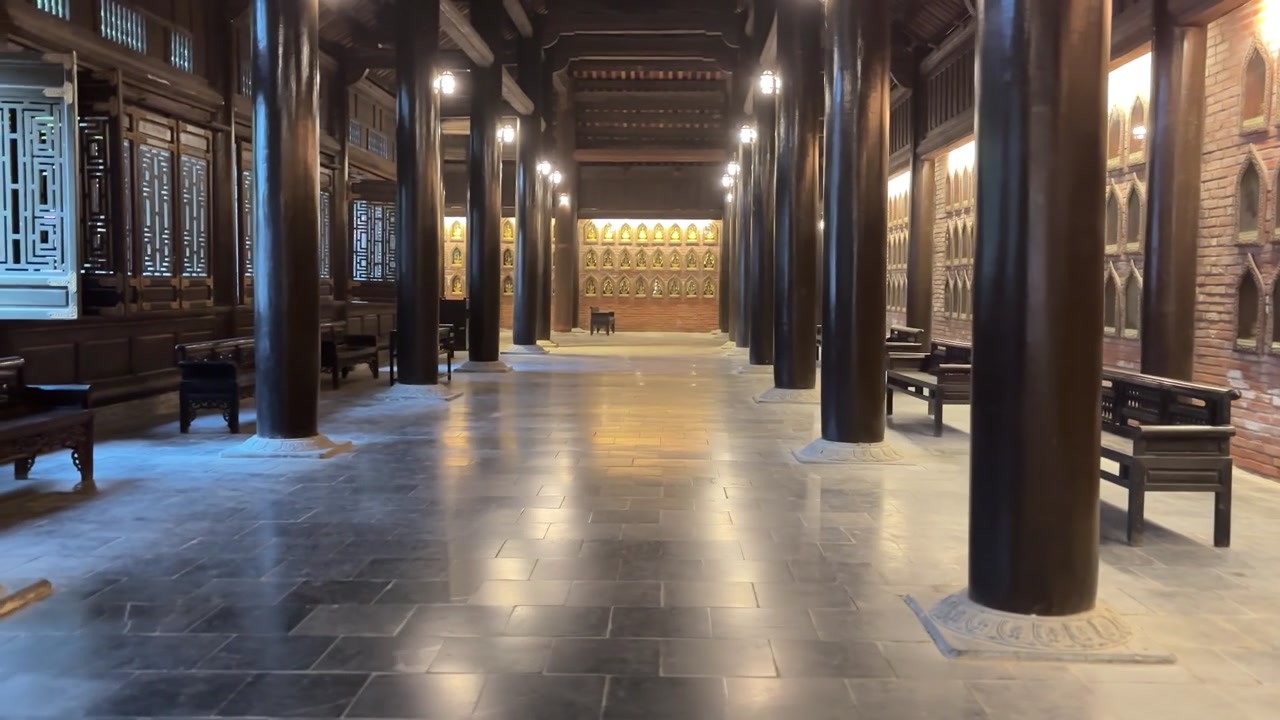 Ninh Binh, Vietnam'daki Bai Dinh Pagodası'nın içinden, koyu renk ahşap sütunlar, Buda nişli tuğla duvarlar ve tapınak salonu boyunca uzanan bankları gösteren bir çekim.