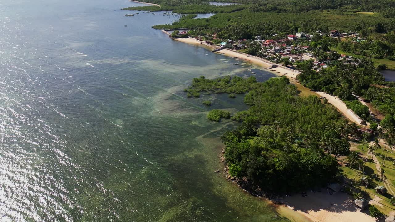 Aerial view of stunning tropical island coastline with lush greenery and quaint village barangay during daytime at San Andres, Catanduanes, Philippines.