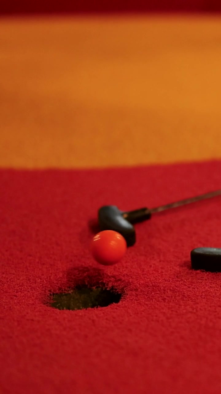 En rød golfbold ruller forbi hullet på en levende rød minigolfbane.