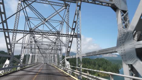 Steel truss spans the Columbia River at Cascade Locks, Oregon. Bridge of the Gods rises above forested hills and flowing water, blending engineering precision with Pacific Northwest grandeur