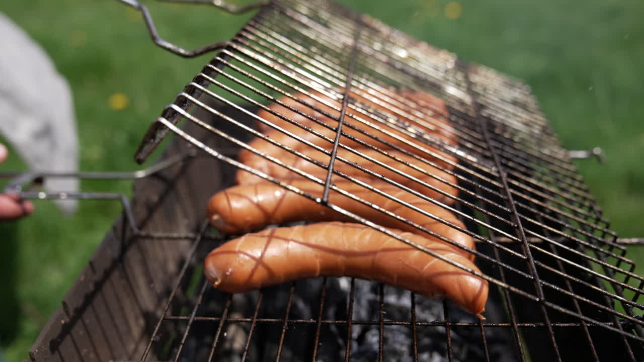 Man putting sausages on the grill. Grilled fresh meat sausages on an open air. Ruddy sausages are fried on charcoal. Close-up.