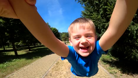 el padre sostiene al niño del niño (hijo) de las manos y gira a su alrededor, una sonrisa en el rostro del niño, emociones brillantes, felicidad.