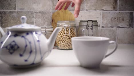 Picking-up-a-Jar-of-Chick-Peas-with-a-Mug-and-Teapot-in-the-Foreground