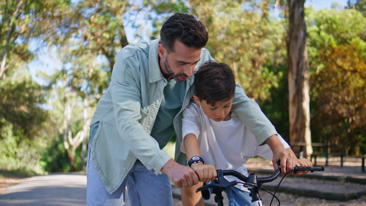 Father teaching son cycling in autumn park closeup. Small boy riding bicycle