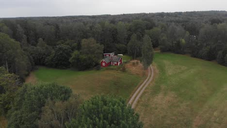 Small-red-wooden-house-in-middle-of-Swedish-forrest,-aerial