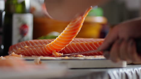chef slicing raw salmon fillet at home for sushi rolls preparation, close-up