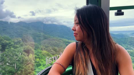 asian woman smiles while riding a cablecar above the rainforest, wet tropics world heritage area