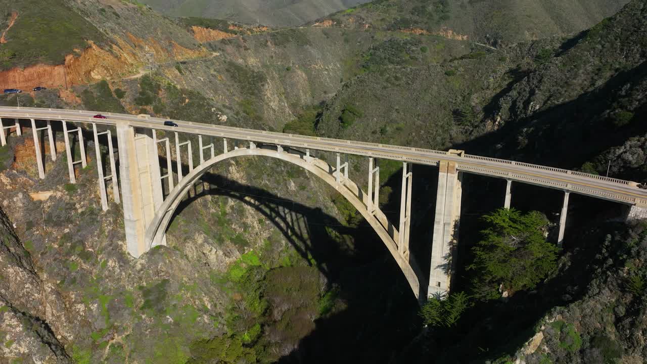 вид с воздуха на мост биксби, когда автомобили проезжают по арочному мосту вдоль шоссе 1 биг-сур, калифорния