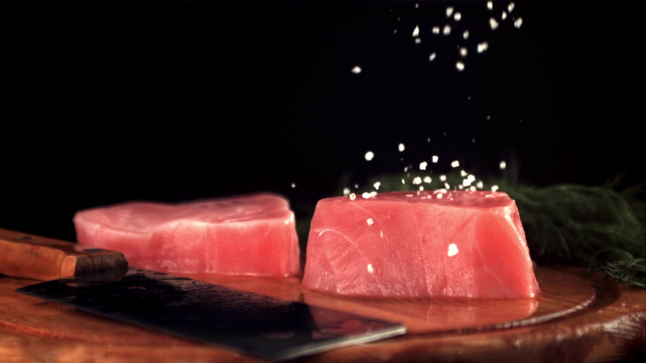 Tranci di tonno crudo che vengono salati su un tagliere di legno