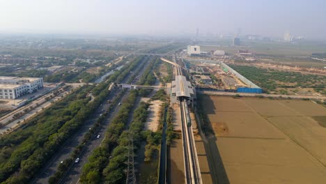aerial drone shot capturing noida metro train along the expressway and farm land