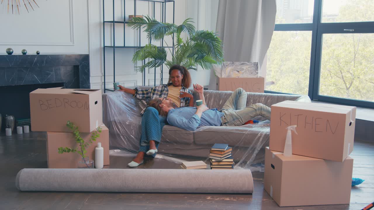 다양한 젊은 부부는 새로운 집으로 이사하고 상자를 내린 후 소파에서 휴식을 취합니다.