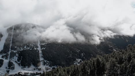 Aerial-panorama-between-trees-of-a-valley-in-cloudy-alpine-snowy-mountain-with-clouds