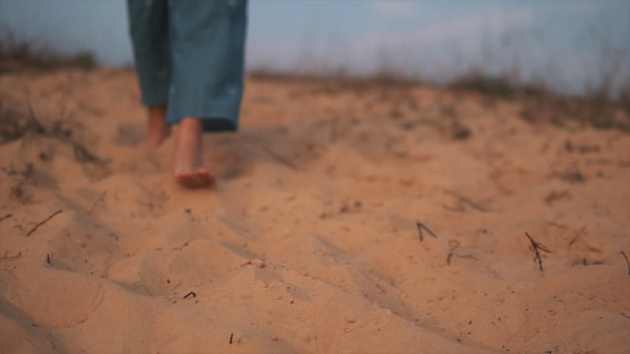 석양에 모래사장에서 맨발로 혼자 걷는 파란 죄수복을 입은 여자