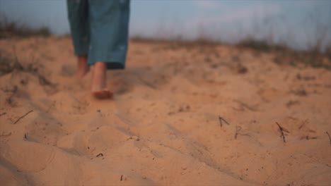 mujer con mono azul caminando descalza y sola en una playa de arena al atardecer