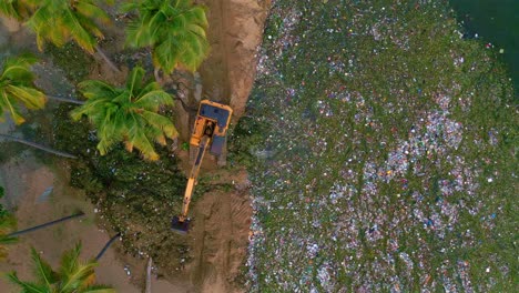 Drone-Vertical-Sobre-La-Cabeza-De-La-Excavadora-Excavando-Plástico-Y-Desechos-Fuera-De-La-Costa---Catástrofe-Ambiental-En-La-Tierra