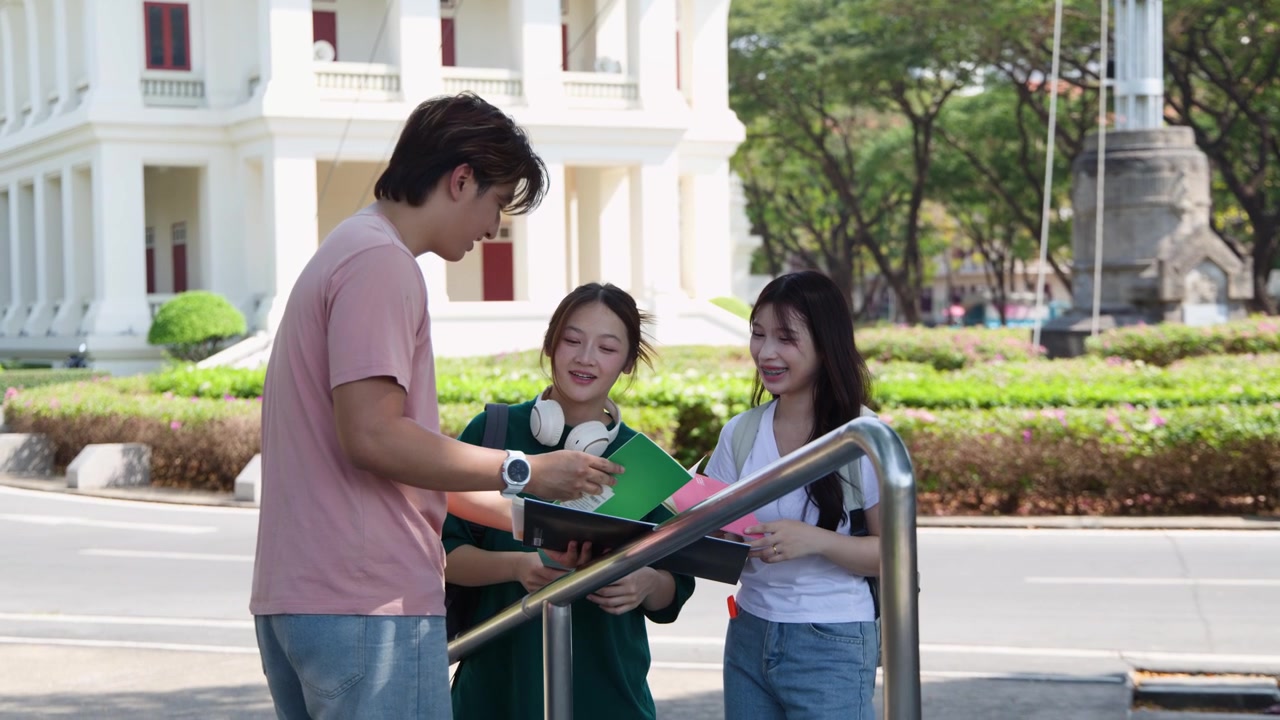 Ba học sinh đứng cạnh lan can, xem lại sổ tay và trò chuyện dưới ánh sáng ban ngày rực rỡ