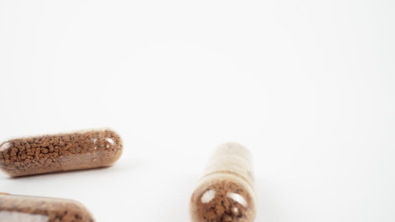 primer plano de dos cápsulas de hierbas en foco agudo contra un fondo blanco brillante