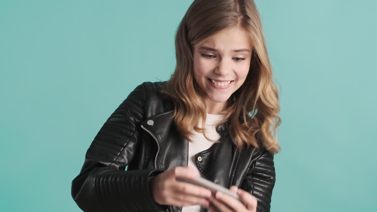 Teenage Caucasian girl in leather jacket playing online games on her smartphone and winning.