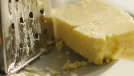 close up with slow focus across freshly grated british mature cheddar cheese resting on side next to grater in soft evening light. rustic classic food setting with cooking ingredients