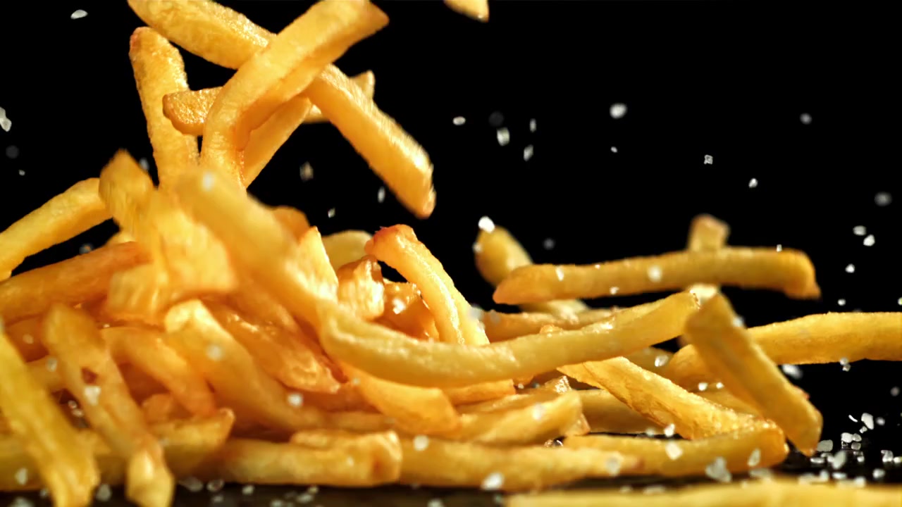Goldene Pommes Frites und Salz fallen auf schwarzen Hintergrund