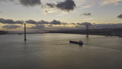 un avión no tripulado se eleva y se aleja de un buque cisterna que se dirige bajo el puente de lisboa.