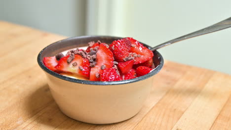 Fresh-cut-up-strawberries-and-cocoa-nibs-in-a-small-bowl-on-wooden-counter