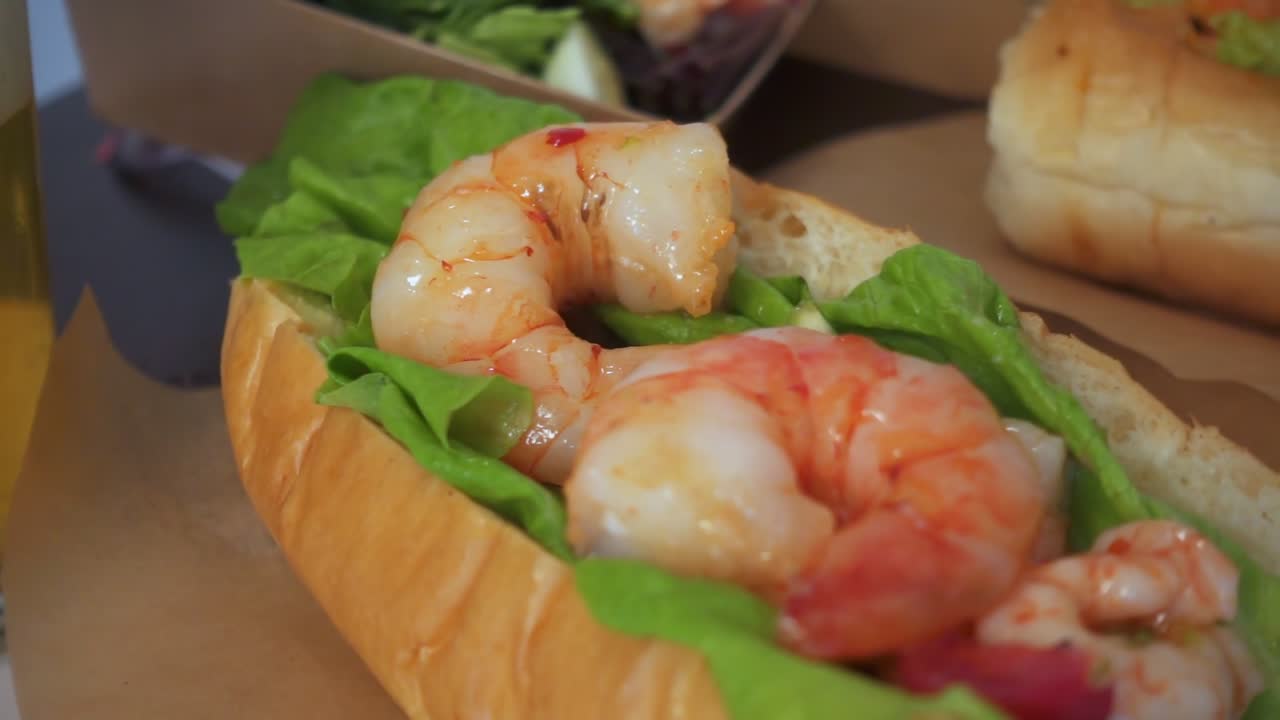 Close-up of a shrimp sandwich with crisp lettuce in a soft bun, highlighting fresh texture and vibrant color in a well-lit food setting.
