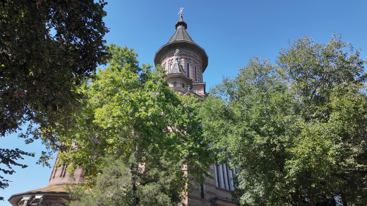 Timisoara’s Metropolitan Cathedral partially obscured by trees, creating a natural frame and picturesque composition