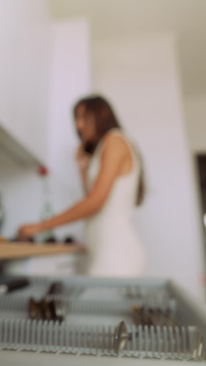 Giovane donna che parla al telefono mentre carica la lavastoviglie in cucina