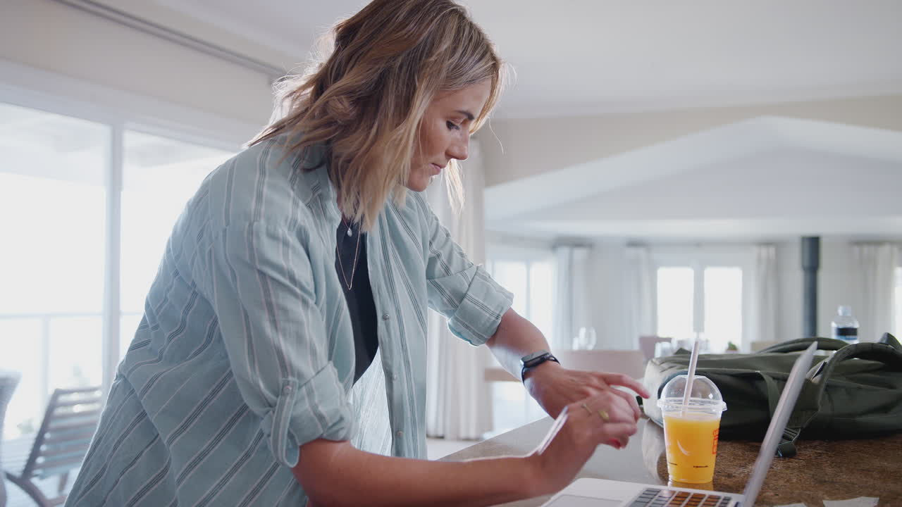 mujer vestida casualmente descargando datos de un rastreador de salud personal a una computadora portátil en casa