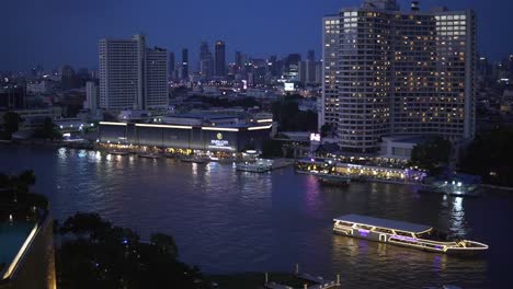 una vista panorámica de la noche del centro de bangkok, tailandia, con luces de la ciudad y un barco turístico que pasa por el río