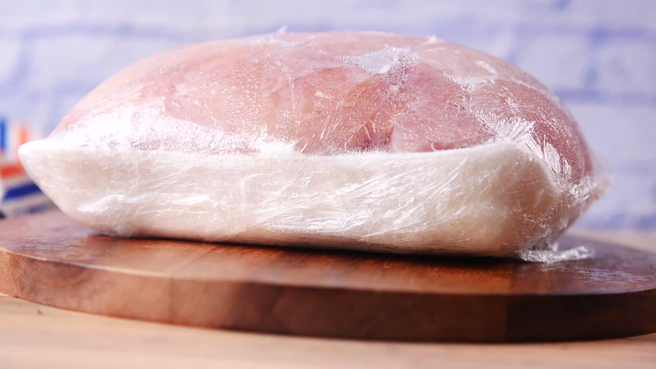 pecho de pollo envuelto congelado en una tabla de cortar de madera