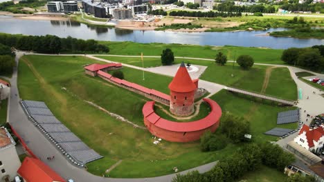 drone shot of the historic old red brick kaunas castle with vytis statue and ukrainian flag near the nemunas river in kaunas old town, lithuania on a sunny day, parallax shot