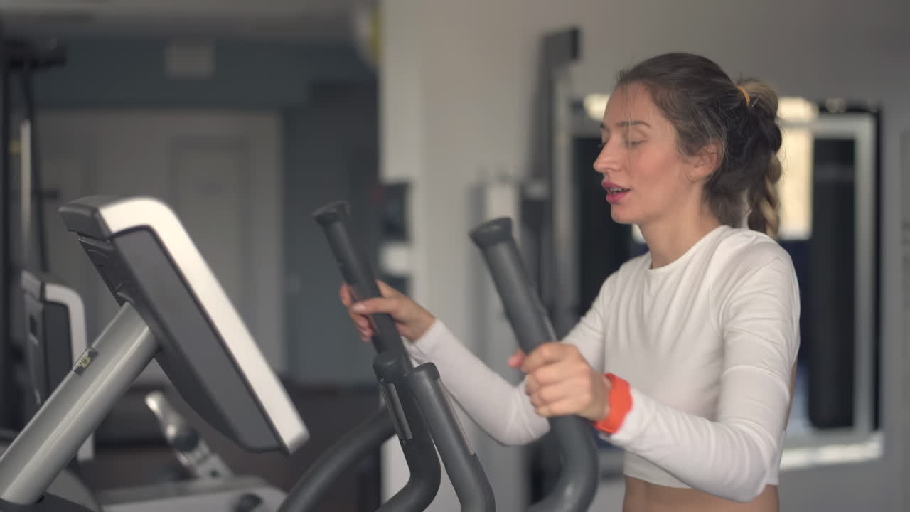Donna in abbigliamento sportivo bianco che si allena sulla macchina ellittica in palestra