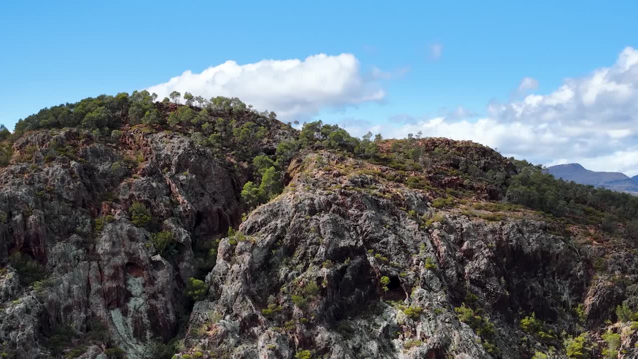 Un drone effettua una panoramica su frastagliate formazioni rocciose e crinali boschivi sotto un cielo azzurro brillante