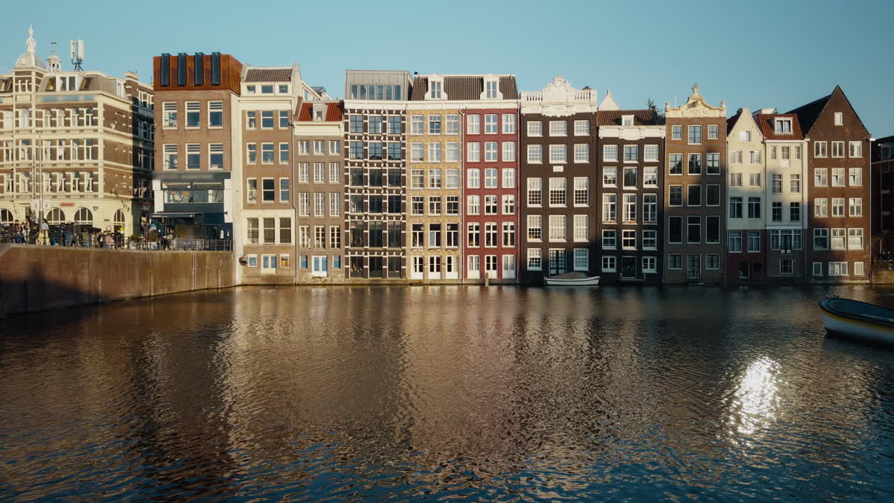 Icónicas casas del canal Damrak en Ámsterdam iluminadas por la luz del sol de la hora dorada y reflejándose en el agua.