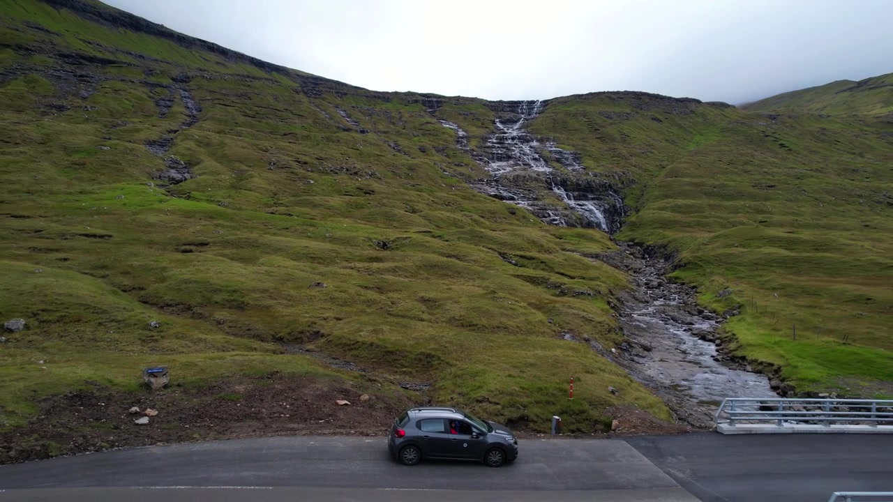 Ripresa aerea che rivela una cascata mozzafiato da un'auto in sosta con persone all'interno, Isole Fær Øer.