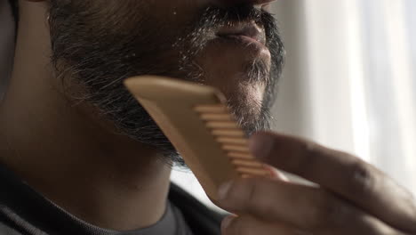 Ethnic-Minority-Adult-Male-Combing-Beard-Near-Curtain-Windows