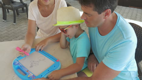 padre e hijo miran a la madre pintando mascotas en el tablero magnético