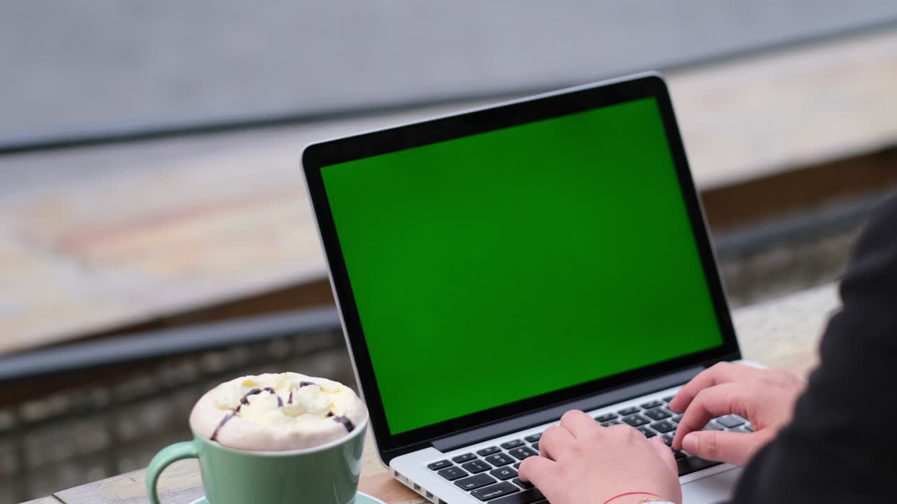 vista a spalla della mano che scrive su un computer portatile a schermo verde in un caffè