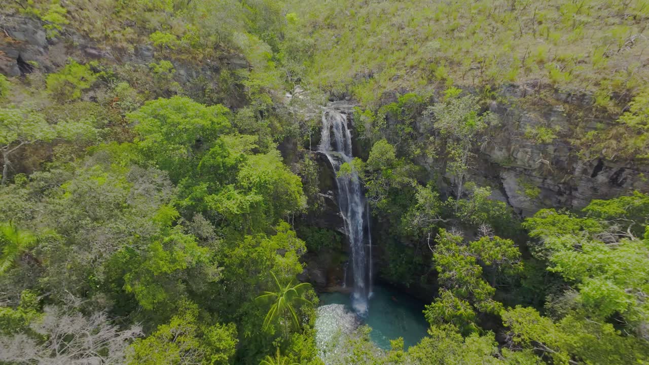 Santa Bárbara waterfall cascading down a rocky cliff surrounded by lush green vegetation in Chapada dos Veadeiros National Park, Goias, Brazil, offering a breathtaking view, fpv drone shot