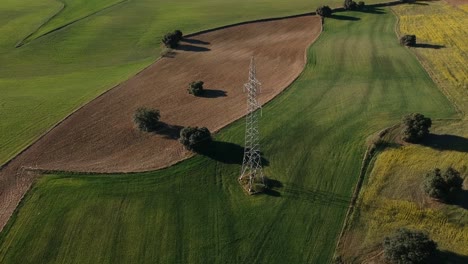 volando alrededor de una torre eléctrica sobre campos arados