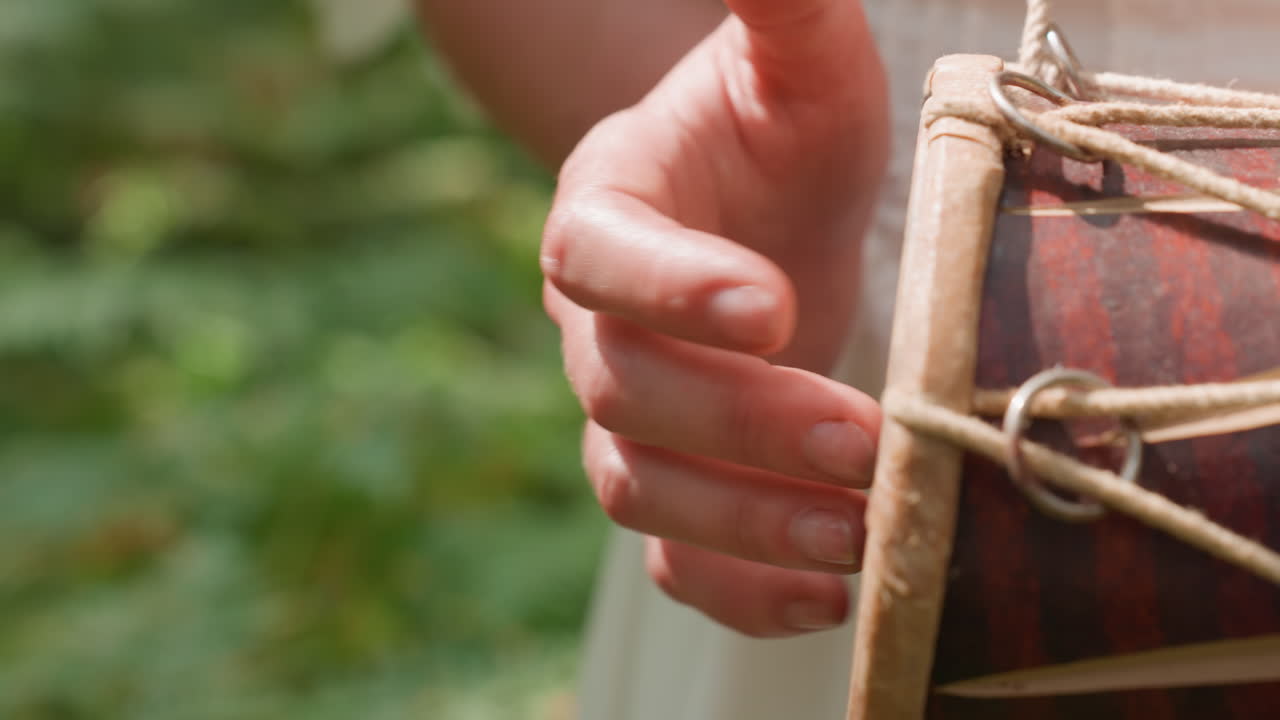 Close up of fairy person tapping drum fast with rhythmic motion, fingers glowing in sunlight against blurred forest background, expressing energy, art, and magical connection