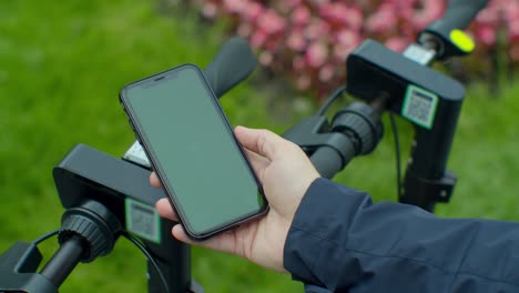 young man paying for electric scooter use app with green mock-up screen smartphone. green screen smartphone.