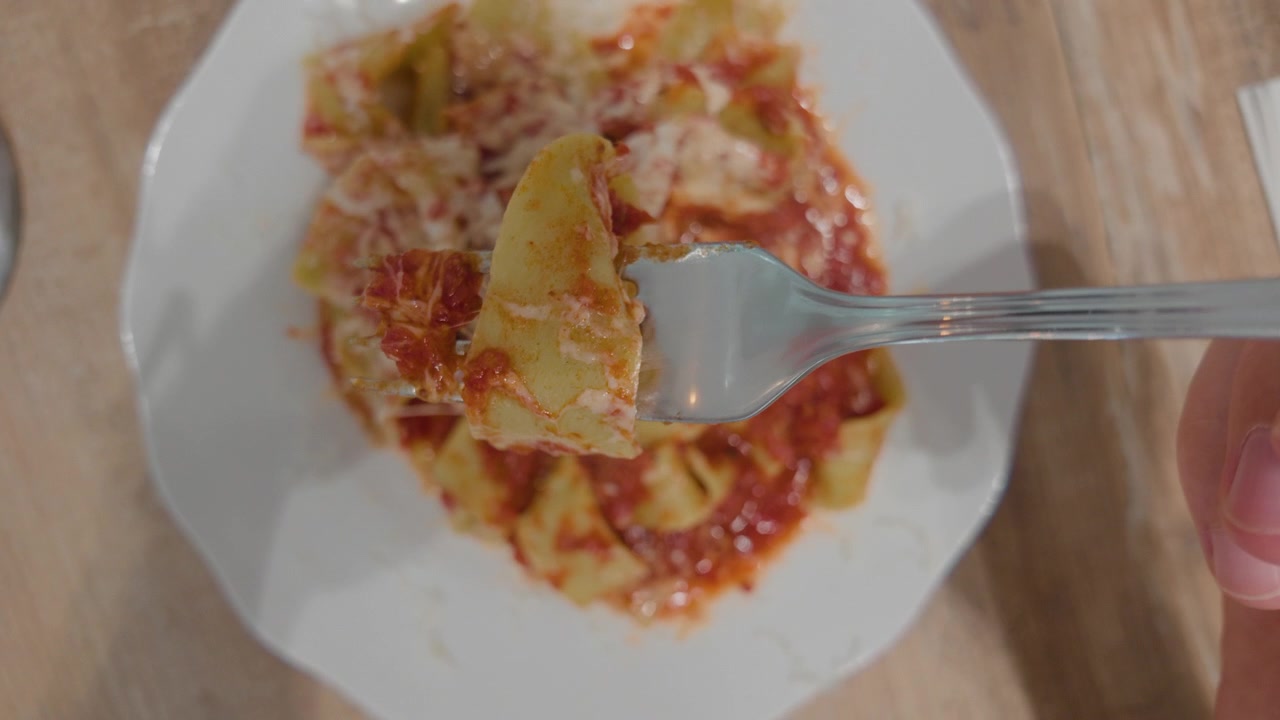 Vista dall'alto di pappardelle al sugo di pomodoro con una forchetta che solleva un boccone