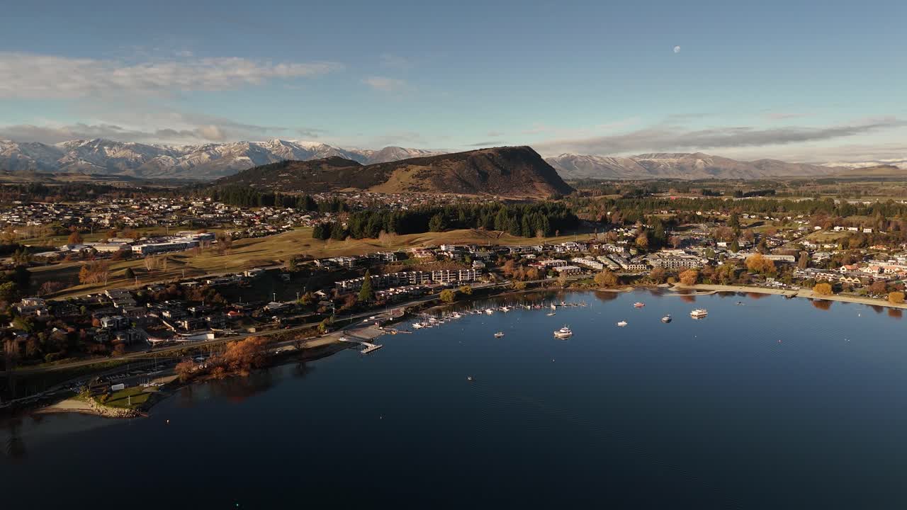 Aerial drone flight over Wanaka city and the surrounding Lake Wanaka in New Zealand, a popular ski and summer resort town highlighting lakeside urban settlement and alpine backdrop