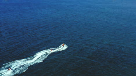 People-riding-on-water-jet-ski-in-blue-sea-aerial-view