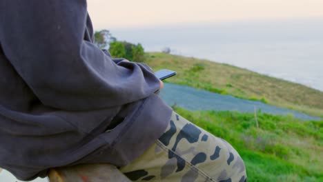 side view of young caucasian male skateboarder texting on mobile phone at observation point 4k